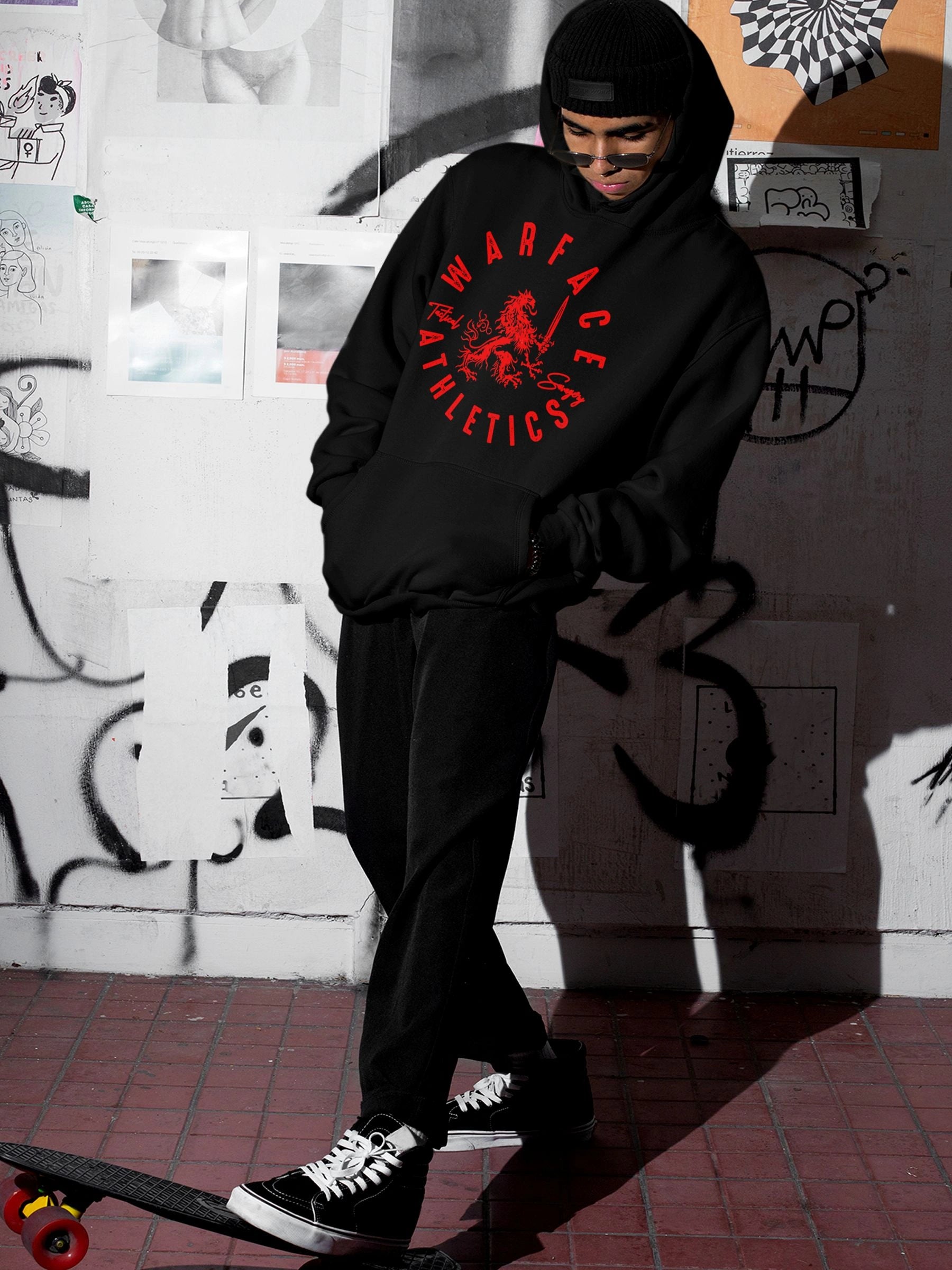 Streetwear model wearing a black hoodie with red Warface Athletics lion logo in front of a graffiti-covered wall