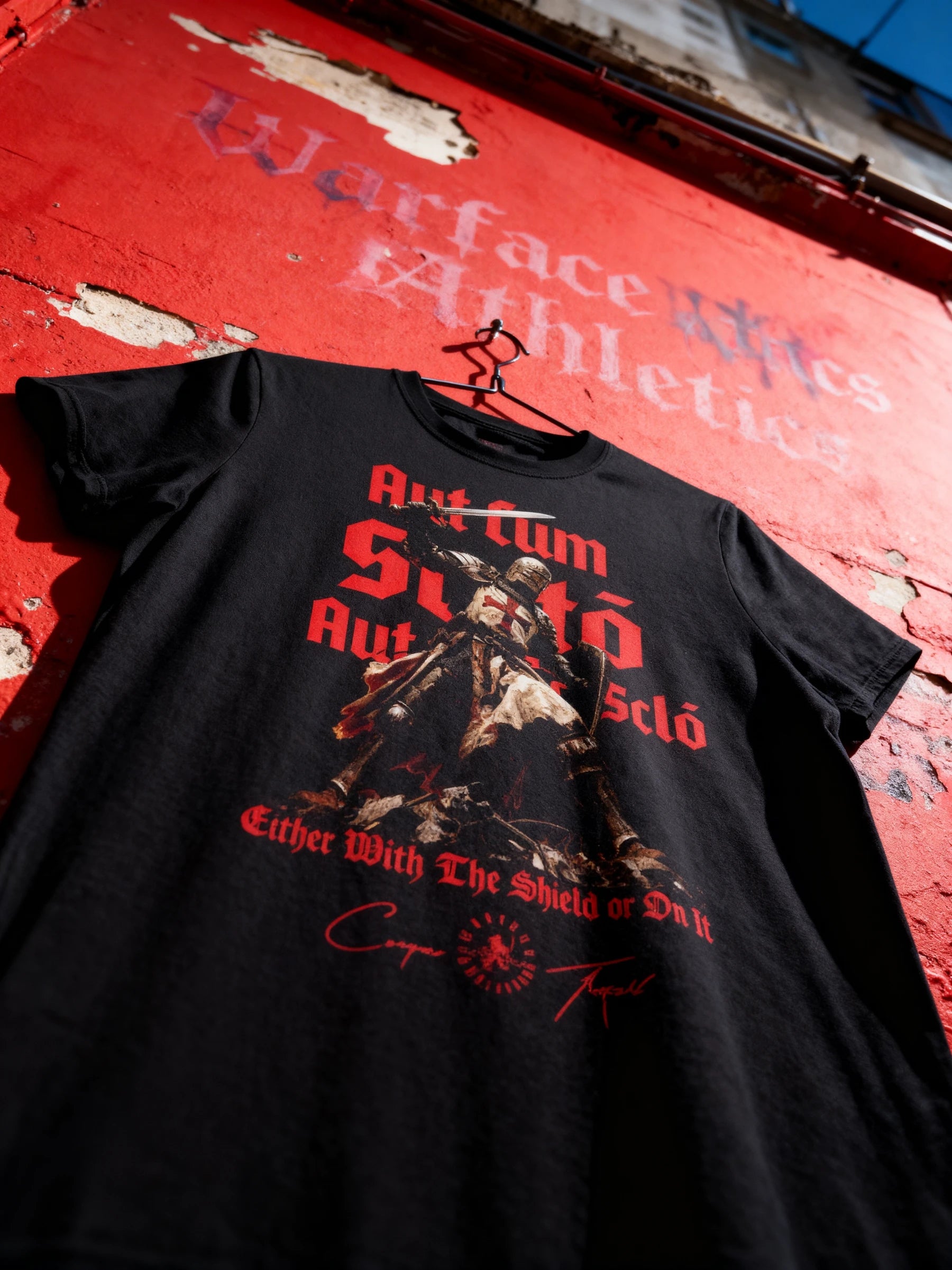 Aut Cum Scuto Aut In Scuto back print – men's black Templar knight gym shirt on red wall, Comfort Colors 1717.