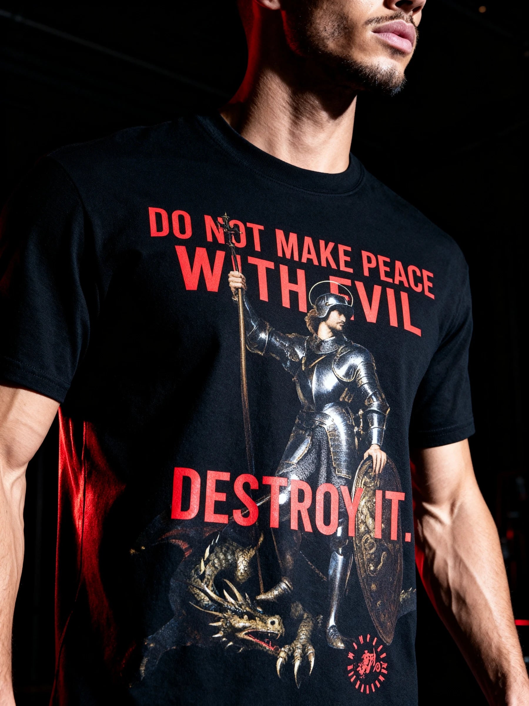 Streetwear model wearing a black St George dragon slayer t-shirt with a warrior knight graphic and stoic text on a dark background