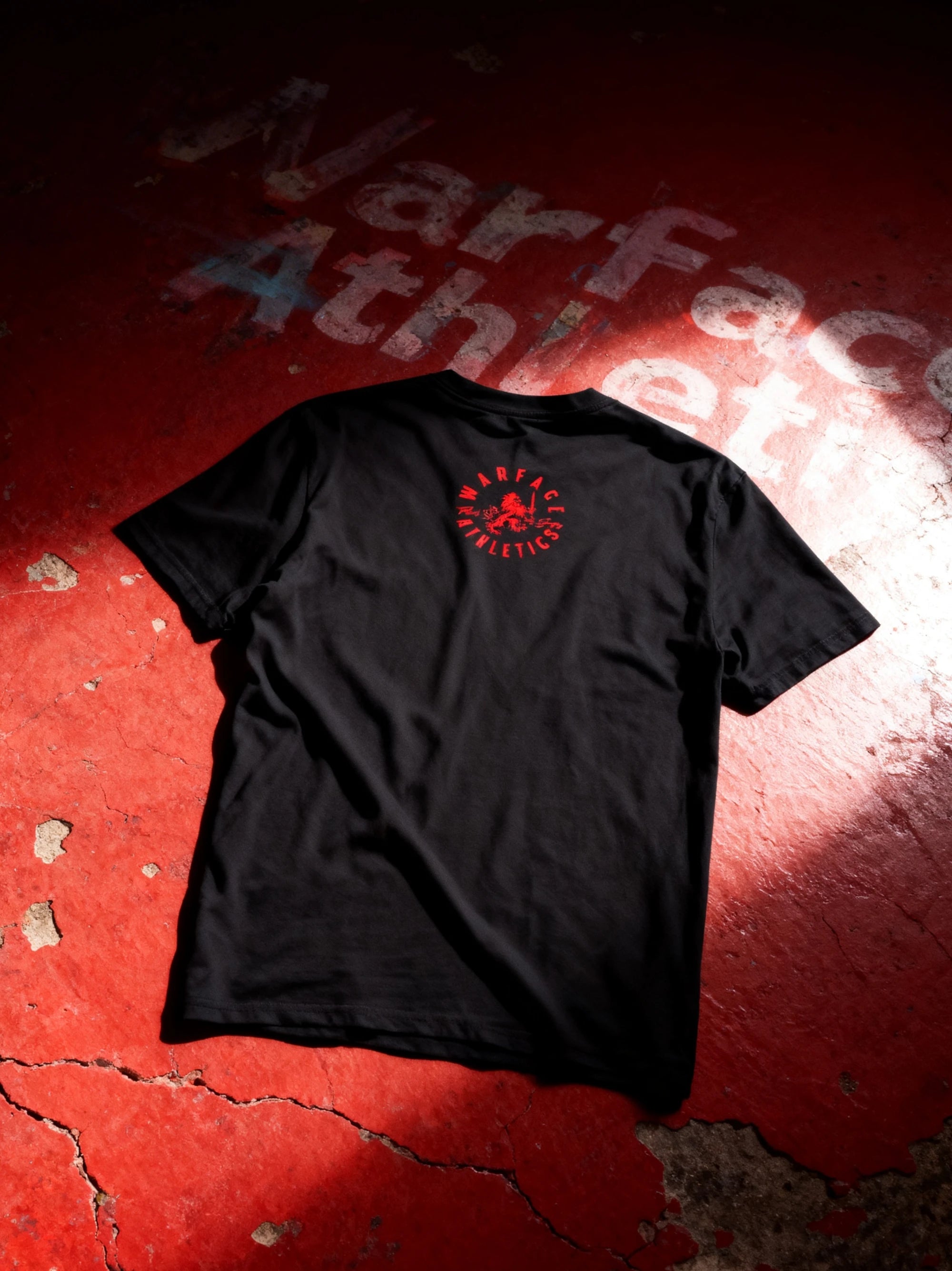 Black gym t-shirt with red warface athletics logo on a red textured floor surface